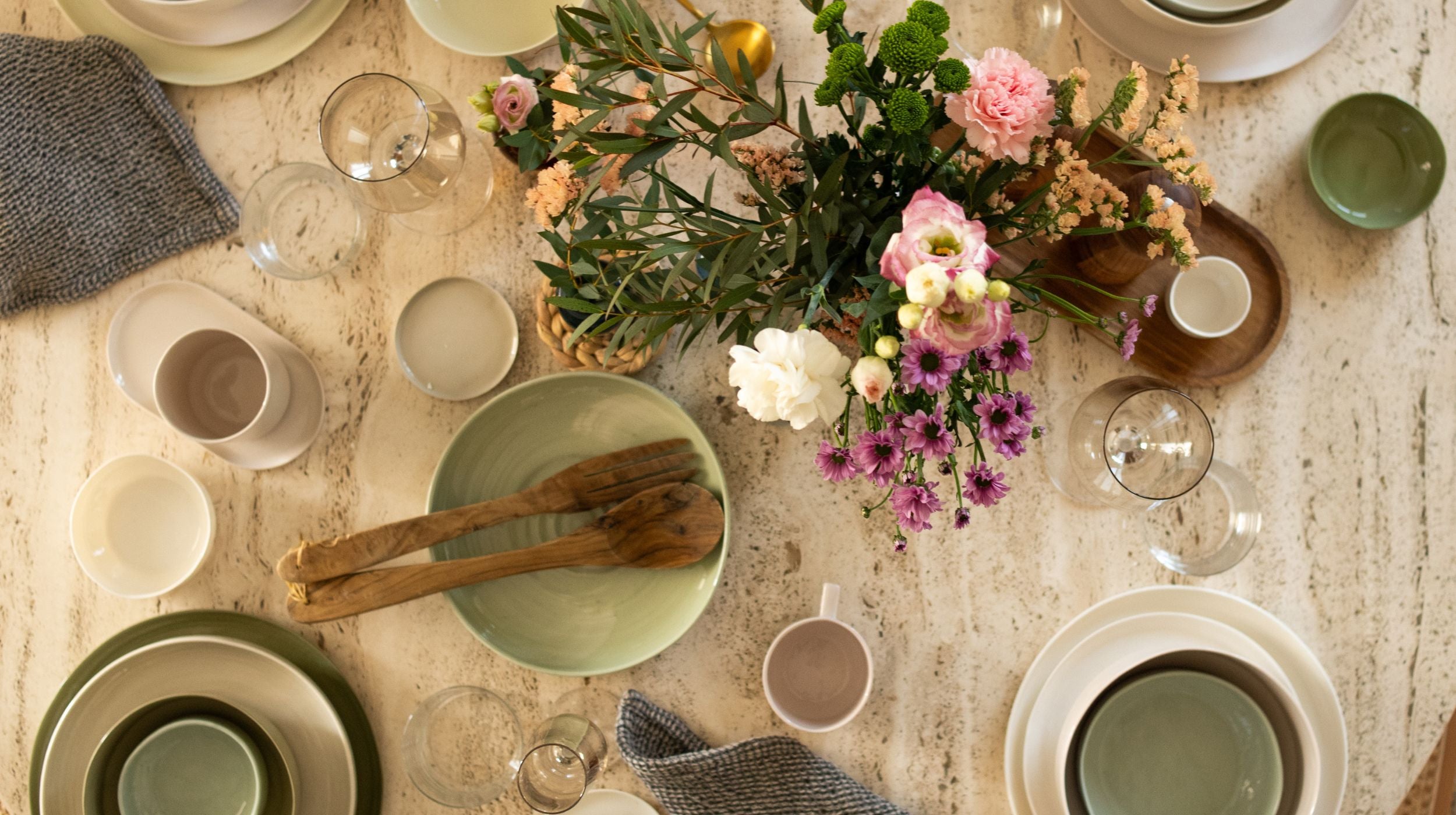 Dining table set with ceramic plates, glasses, and a floral centerpiece on a wooden surface.