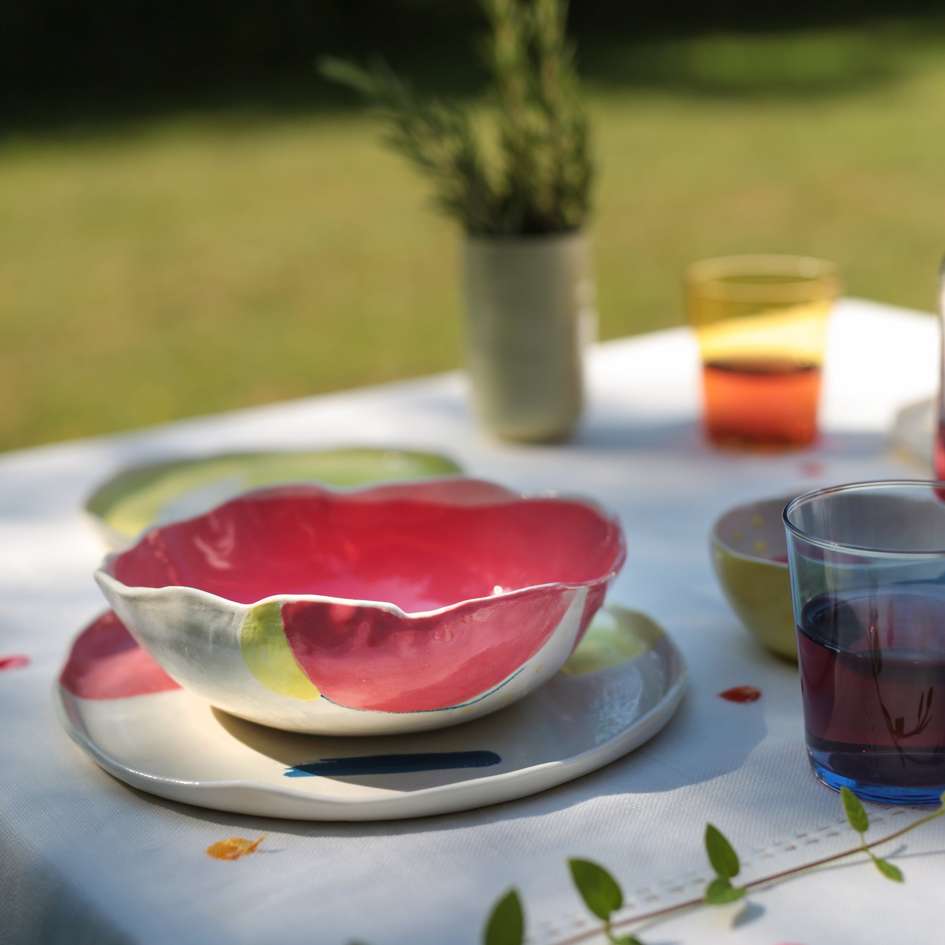 A colorful porcelain bowl with a floral design, predominantly red, displayed on a table with other dinnerware in the background.